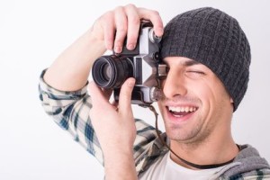 Young smiling photographer with camera on the gray background.